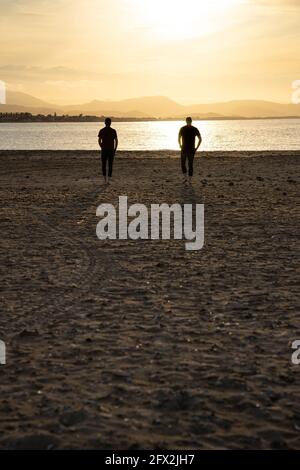 Zwei Männer, die auf das Meerwasser zulaufen. Bei Sonnenuntergang. Sie gehen auseinander. Stockfoto