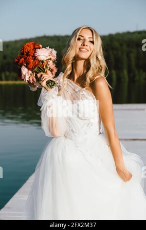 Elegante blonde Braut in Weiß mit einem Hochzeitsstrauß gekleidet. Hochzeitskonzept Stockfoto