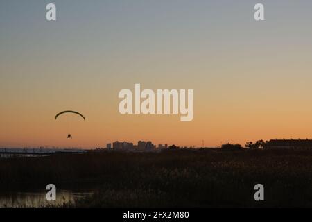 Silhouette eines Gleitschirms, der gegen den orangen Himmel fliegt Stockfoto