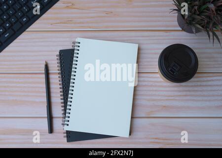 Arbeitsplatz im Home Office mit schwarzer Tastatur, Notizbüchern, Stift, Einweg-Kaffeetasse und Topfpflanze. Flach liegend, Draufsicht Stockfoto