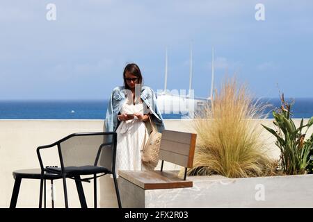 Monte-Carlo, Monaco - 16. Juni 2019: Schöne junge Brünette Frau mit Sonnenbrillen Blick auf ihr Smartphone mit EINER Mega Yacht im Hintergrund in M Stockfoto