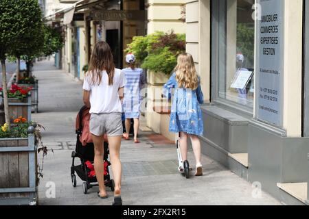 Monte-Carlo, Monaco - 16. Juni 2019: Rückansicht einer jungen Mutter, die ihren Kinderwagen auf der Straße mit ihrer Tochter im Motorroller in Monte-carlo schiebt, Stockfoto