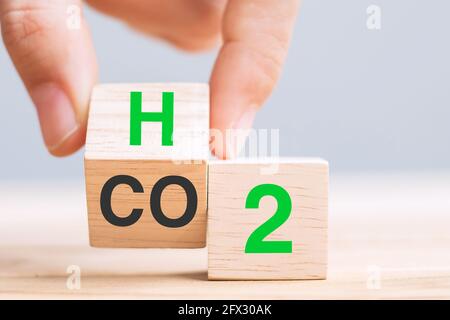 Holzwürfelblöcke von Hand mit CO2 (Kohlendioxid) umklappen, in den Text H2 (Wasserstoff) auf dem Tabellenhintergrund wechseln. Freier Kohlenstoff, alternative Energie und Glob Stockfoto