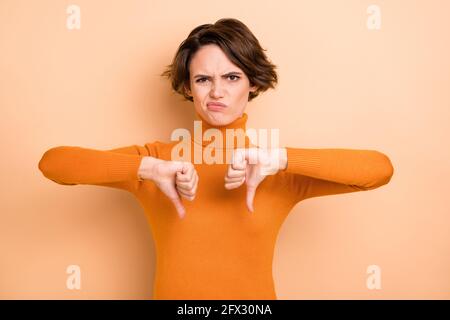 Foto von charmanten traurig junge Dame tragen orange Rollkragen zeigt Daumen nach unten zwei Hände Arme isoliert beige Farbe Hintergrund Stockfoto