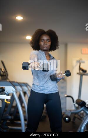 Frau beim Training mit Hanteln im Fitnessstudio zu Hause. Nahaufnahme, eine Person, Fitnessmodell, afroamerikanisch, afrikanisches Modell, Sportbekleidung, Naturhaar-Modell Stockfoto