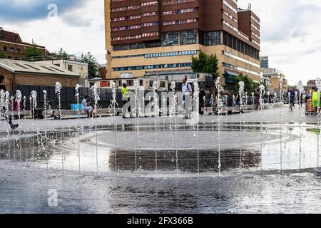 Niedrige Ebene, Blick auf die Fontäne des Paddington Basin mit Menschen, die sich amüsieren - mit Springbrunnen Jets, Reflections und modernen Gebäuden. Stockfoto