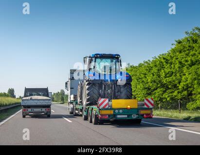Neuer blauer Traktor auf langer Anhängerplattform für den Transport schwerer Maschinen auf der Autobahn. Transport von Landmaschinen Stockfoto