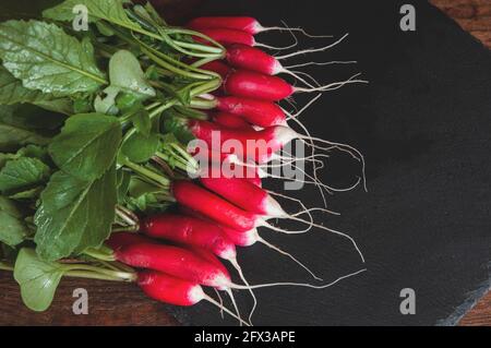 Frischer Rettich mit Stielen und Blättern liegt auf einem schwarzen Podest-Brett aus Granit Stockfoto