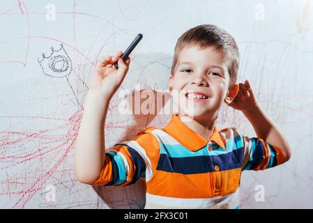 Lachendes Kind zeichnet mit Buntstiften an die Wand Stockfoto