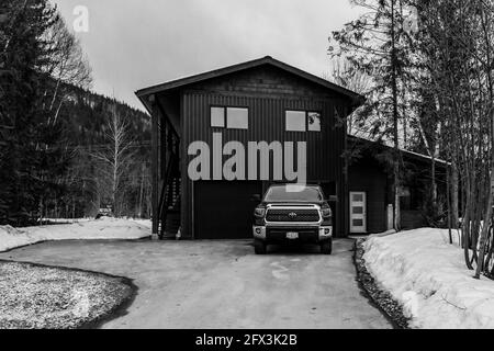 REVELSTOKE, KANADA - 14. MÄRZ 2021: Schwarz-weißes Privathaus in Kleinstadt Abendzeit früher Frühling mit Schnee Stockfoto