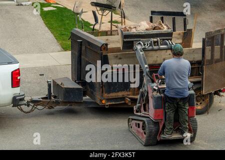 Der Traktorfahrer brachte in einem Eimer große Steine von der Baustelle und belädt sie in den Anhänger. Stockfoto