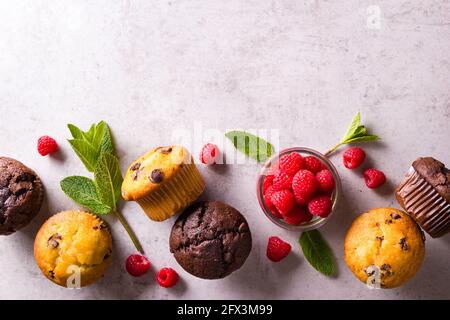 Goldene und braune Muffins zwischen frischer Minze, die um einen herum angeordnet sind Glas mit frischen Himbeeren auf grauer Arbeitsplatte Stockfoto