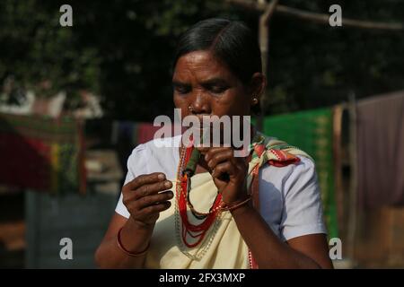 LANJIA SAORA TRIBE - Tribal Woman smoking chilam pipe made of leaves. Runde Holzstopfen oder Taitalya in den Ohren und Khagla- und Jatong-Schmuck um sie herum Stockfoto