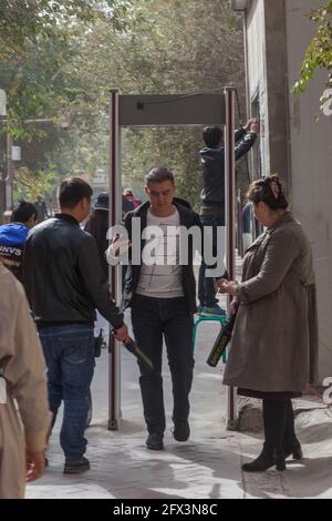 Junger Mann, der in der Volksrepublik China durch den Sicherheitszugang auf der Hauptlebensmittelstraße von Kashgar geht Stockfoto