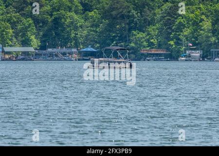 Ein Mann, der ein Pontonboot mit einer Überdachung fährt Langsam legt das schwimmende Boot an der Küste von an Der See an einem hellen, nebligen Tag im späten spr Stockfoto