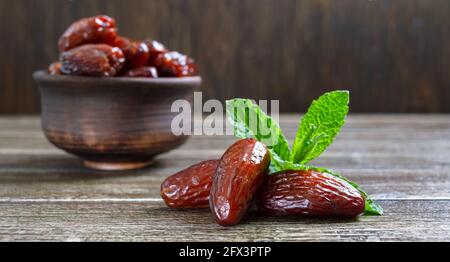 Sonnengetrocknete Datteln Früchte und frische Minzblätter in einer Keramikschale auf einem Holztisch. Nahaufnahme Stockfoto