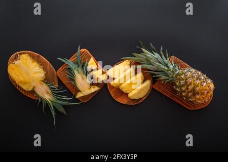 In Scheiben geschnittene Ananas in verschiedenen Formen. Reife Ananas auf Schneidebrett Kochen Sommer Dessert auf schwarzem Hintergrund. Flach liegend Stockfoto