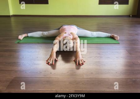 Eine Frau in Sportbekleidung, die Yoga praktiziert, führt eine Samokanasana-Übung auf einer Matte durch, einem Querstrang mit einer Neigung des Körpers nach vorne. Stockfoto