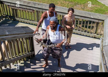 CYPREMORT POINT, LA, USA - 15. MAI 2021: Fischer mit kleinem Alligator, den er in Shark Bayou gefangen hat, gehen mit zwei Freunden Treppen hinauf. Stockfoto