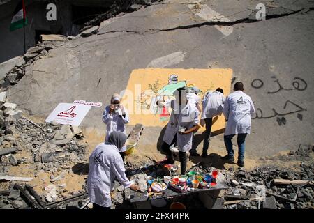 25. Mai 2021: Gaza, Palästina. 25 Mai 2021. Palästinensische Künstler malen ein Wandgemälde mit dem Titel „siegreiches Palästina“ über die Ruinen des Al-Shuruq-Turms, das am 21. Mai durch israelische Kampfflugzeuge auf Gaza-Stadt durch Luftangriffe zerstört wurde. Während der jüngsten 11-tägigen Konfrontation zwischen Israel und den palästinensischen Gruppierungen im Gazastreifen wurde Gaza ständig mit Luftangriffen und Artilleriebüllen angegriffen, was viele Opfer und Zerstörung verursachte. Mehrere Raketen wurden aus dem Gazastreifen auf Israel abgefeuert, und obwohl die meisten von ihnen abgefangen und zerstört wurden, ereigneten sich in Israel einige Verletzte. Der Stockfoto