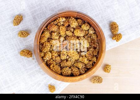 Draufsicht auf getrocknete süße natürliche Maulbeerbeeren in der runden Holzschale auf hellem Hintergrund in der Küche. Stockfoto