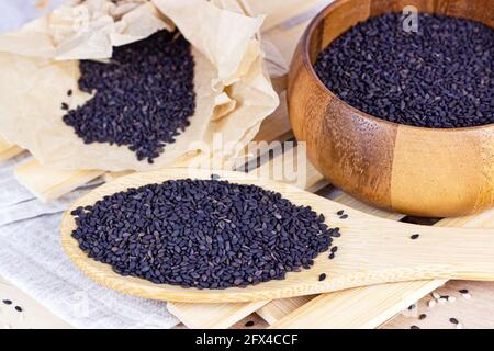 Schwarze Sesamsamen in einem Holzlöffel zum Kochen auf hellem Hintergrund in der Küche. Stockfoto