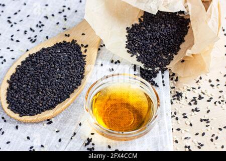 Schwarze Sesamsamen in einem Holzlöffel und Öl auf Heller Hintergrund in der Küche Stockfoto