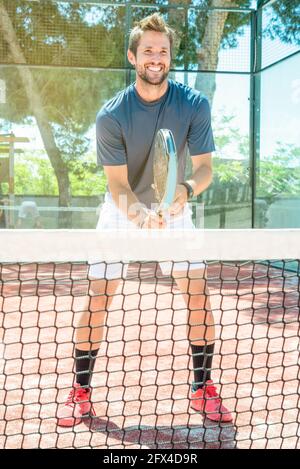 Fröhlich lächelnder junger Mann spielt Tennis unter freiem Himmel gericht Stockfoto