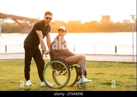 Hilfe für Menschen mit körperlichen Behinderungen. Mann fahren Rollstuhl und helfen seinem Freund. Soziale Dienste für die Bevölkerung. Stockfoto