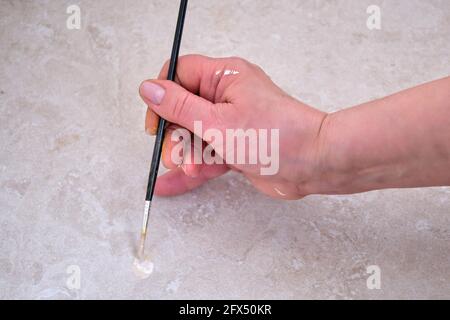 Eine ältere Frau mit einem Pinsel malt Fliesen auf dem Küchenboden. Lackierung zur Wiederherstellung der beschädigten Bodenoberfläche Stockfoto