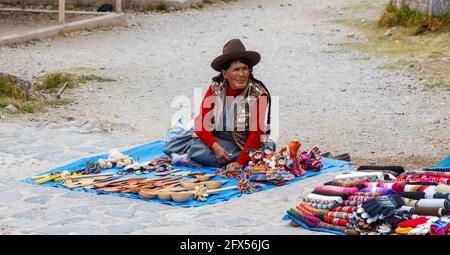 Eine alte Frau in einheimischer Kleidung sitzt am Straßenrand und verkauft touristische Souvenirs, Chinchero, ein Andendorf im Heiligen Tal, Urubamba, Cusco Region, Peru Stockfoto