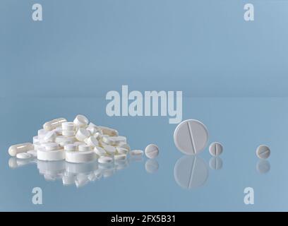 Ein Berg aus weißen Pillen auf blauem Hintergrund und einzelnen großen und kleinen Rollen auf einer reflektierenden Oberfläche. Stockfoto