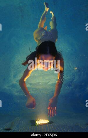 Brunette weibliche Schwimmen im Spa-Pool mit geothermischem Wasser. Schöne Baderin greift mit ihren Händen zu beleuchteten Lichtern aus der Poollampe in der Nacht. Stockfoto