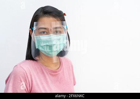 Porträt einer asiatischen Frau mittleren Alters, die medizinische Gesichtsmaske und Gesichtsschutz trägt, schwarzes kurzes Haar und T-Shirt trägt, auf Kamera schaut, isoliertes Bild Stockfoto
