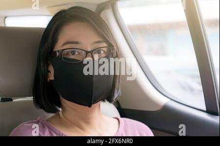 Porträt einer asiatischen Passagierin im Taxi, sitzend auf dem Rücksitz. Tragen schwarze Farbe Gesichtsmaske, um Virus zu schützen, schwarze kurze Haare, tragen Brillen Stockfoto