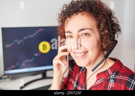 Weibliche Händler operiert mit Bitcoins von ihrem Stehtisch aus Sprechen über das Mobiltelefon und Tragen eines Headsets Stockfoto