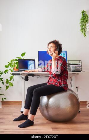 Frau mit Telearbeit, die vor ihr auf einem Fitball sitzt Schreibtisch, der über ein Headset spricht Stockfoto