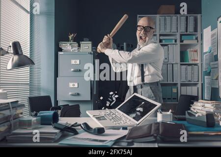 Verrückter gestresster Geschäftsmann zerstört seinen Schreibtisch und Laptop mit einem Baseballschläger, Job Burnout Konzept Stockfoto