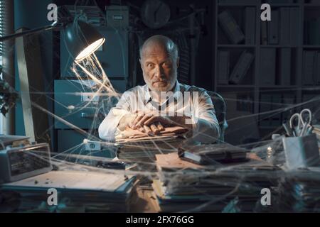 Gestresster verzweifelter Manager, nachdem das Geschäft geschlossen wurde, sitzt er am Schreibtisch im verlassenen Büro Stockfoto