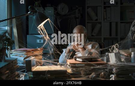 Verzweifelter Geschäftsmann, der in seinem verlassenen Büro am Schreibtisch sitzt: Geschäftsversagen und Konzept der Finanzkrise Stockfoto