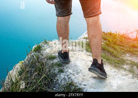 Typ in Shorts am Rand einer Klippe, die Beine aus der Nähe. Stockfoto