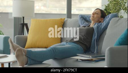 Frau, die eine Pause macht und sich auf der Couch ausruht, schläft mit den Händen hinter dem Kopf Stockfoto