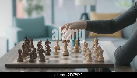Frau, die zu Hause Schach spielt, bewegt eine Spielfigur auf dem Schachbrett Stockfoto