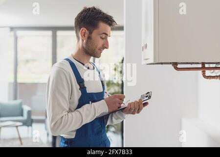 Professioneller Klempner, der einen Kessel bedient und auf einem Klemmbrett schreibt Stockfoto