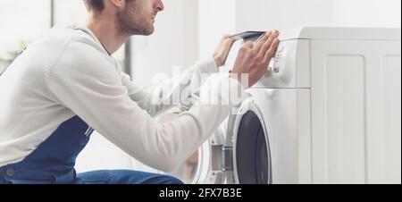Der Mechaniker, der eine Waschmaschine repariert, stellt einen Knopf auf dem Bedienfeld ein Stockfoto