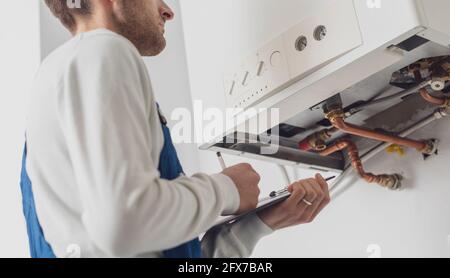 Professioneller Klempner, der einen Kessel bedient und auf einem Klemmbrett schreibt Stockfoto