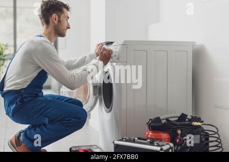 Der Mechaniker, der eine Waschmaschine repariert, stellt einen Knopf auf dem Bedienfeld ein Stockfoto