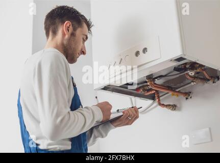 Professioneller Klempner, der einen Kessel bedient und auf einem Klemmbrett schreibt Stockfoto