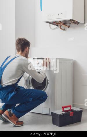 Der Mechaniker, der eine Waschmaschine repariert, stellt einen Knopf auf dem Bedienfeld ein Stockfoto