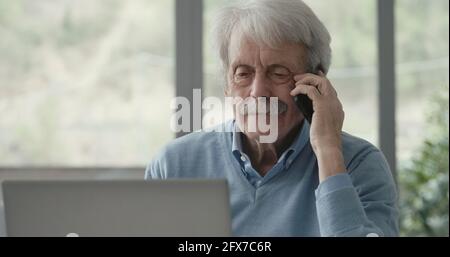 Glücklicher älterer Mann, der an der Rezeption saß und ein Telefon erhielt Rufen Sie auf seinem Smartphone an Stockfoto